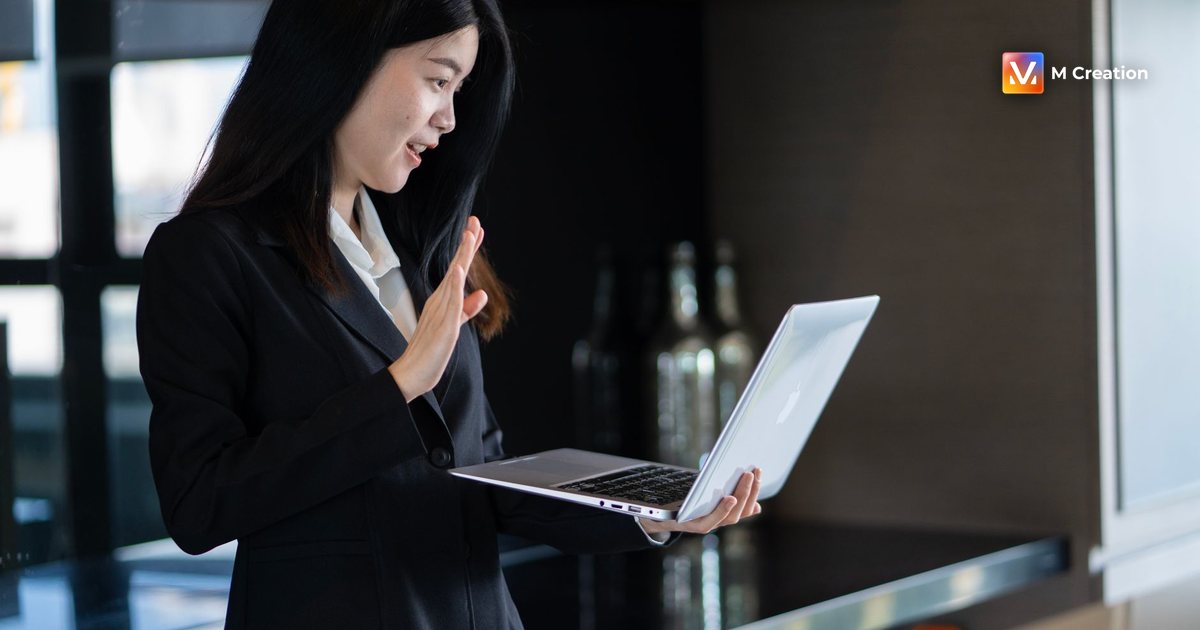 Confident young woman in a black suit engaged in a video call from a home office.