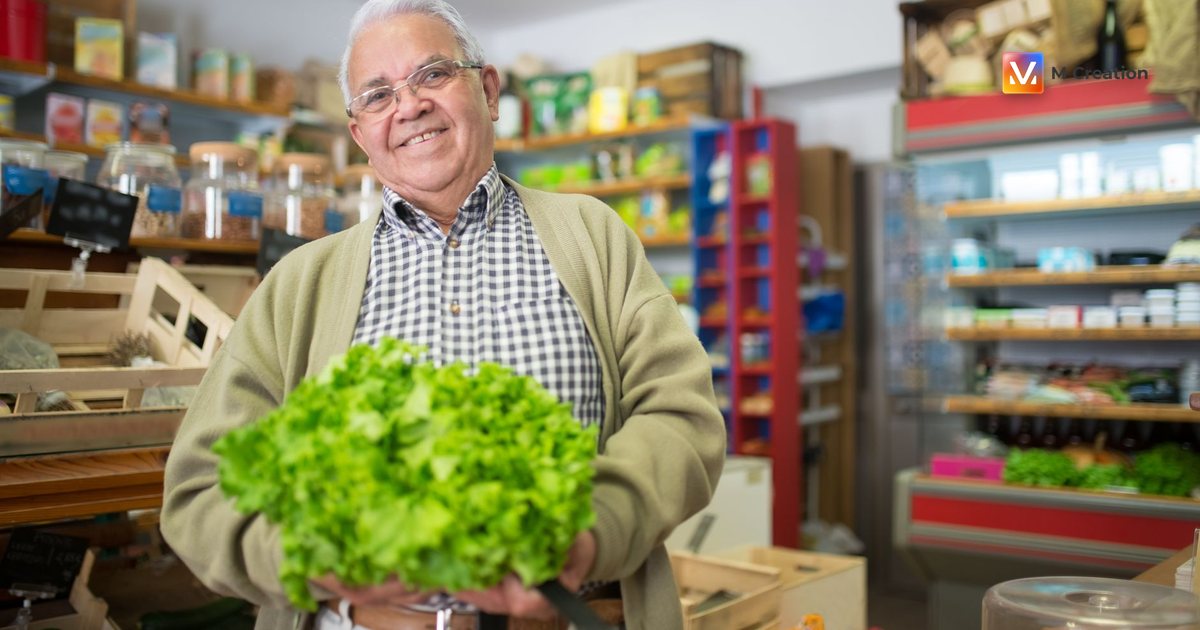 Elderly man with gray hair holding fresh lettuce smiling in a grocery store.